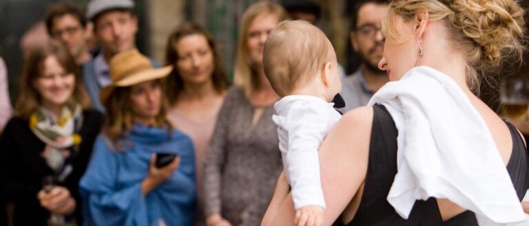 Gäste einer Namensfeier im Freien, eine Frau hält ein Baby im Arm