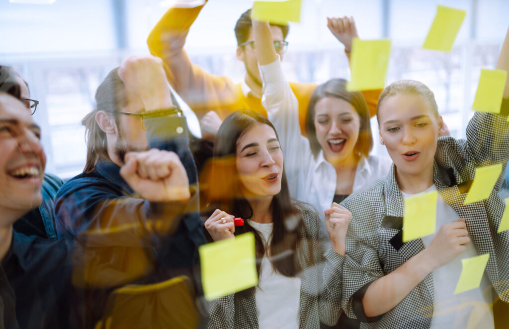 Junge Menschen sammeln gemeinsam Ideen an einer Wand mit Notizzetteln