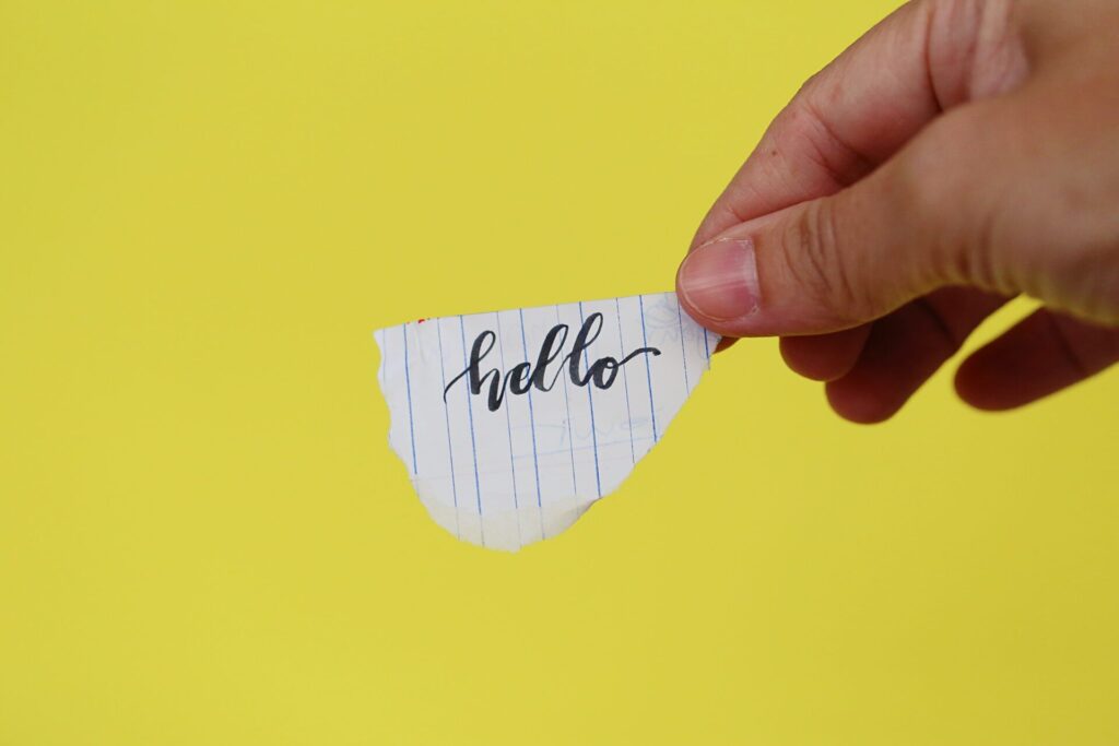 Hand hält einen Zettel mit der handgeschriebenen Aufschrift „hello“